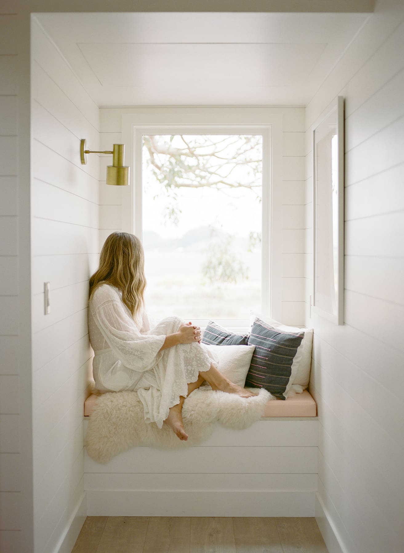 Woman sitting in a window nook looking outside, taking a quiet moment to herself